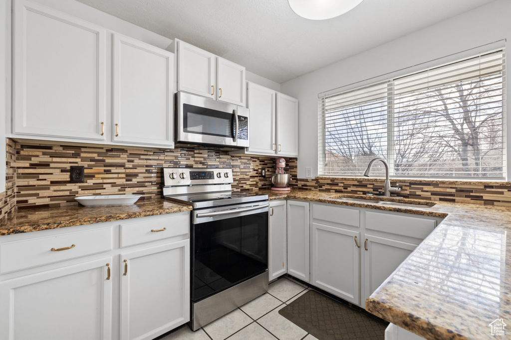 Kitchen featuring stainless steel appliances, tasteful backsplash, white cabinets, and a sink