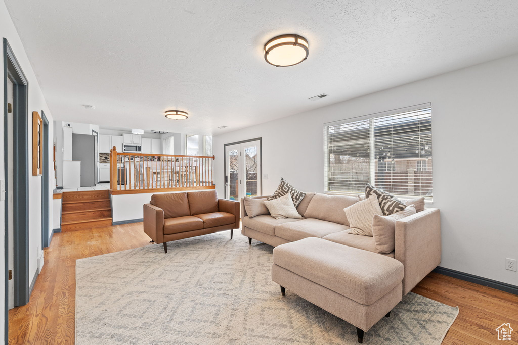 Living room featuring light wood finished floors, baseboards, visible vents, and stairway