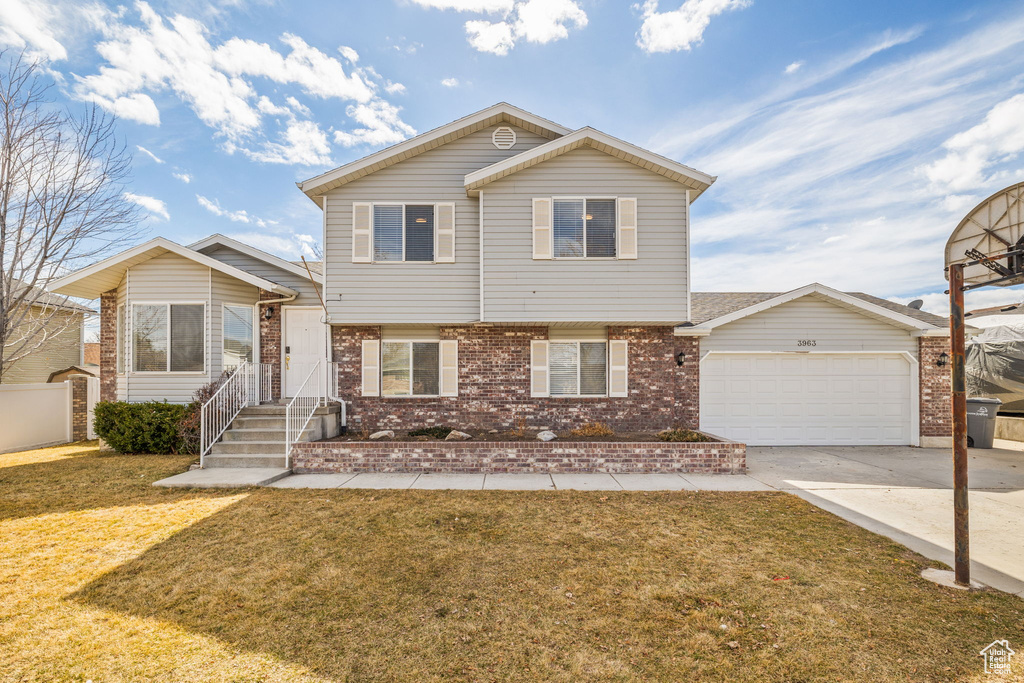 Tri-level home featuring concrete driveway, brick siding, a front lawn, and an attached garage