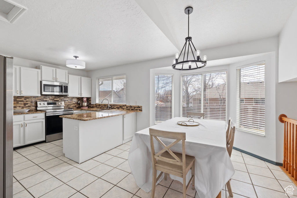 Kitchen featuring an inviting chandelier, white cabinetry, a kitchen island, light tile patterned flooring, and appliances with stainless steel finishes