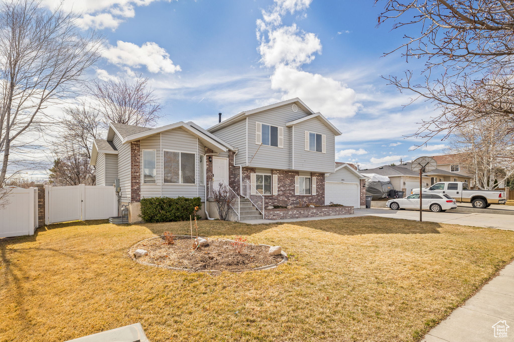 Split level home with a gate, driveway, a front yard, brick siding, and fence