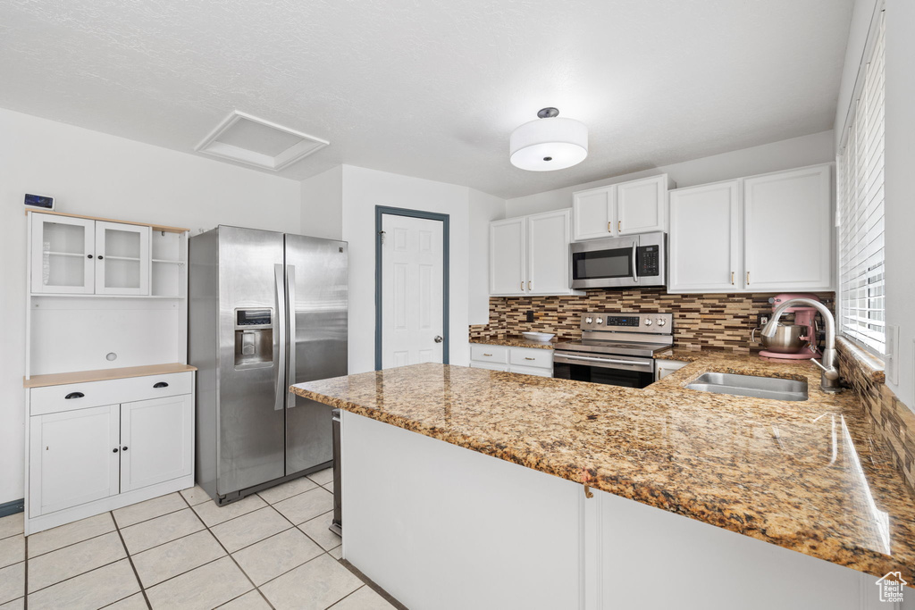 Kitchen featuring stainless steel appliances, a peninsula, a sink, and light stone counters