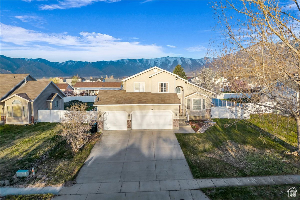 Ranch-style home with a mountain view, concrete driveway, fence, stucco siding, and a front lawn