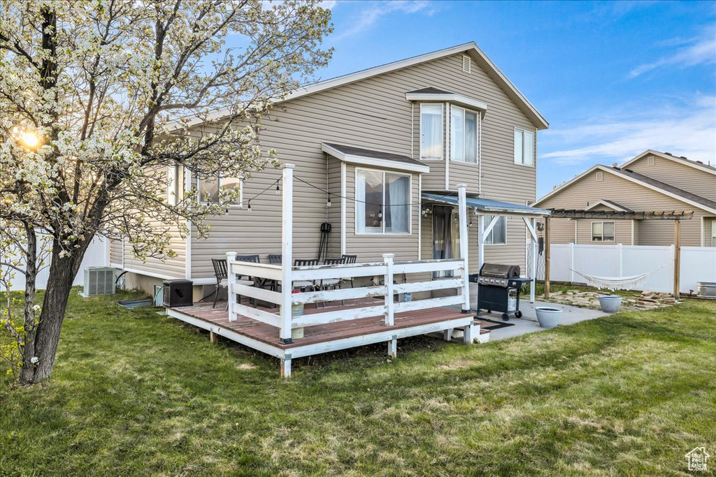 Rear view of property featuring fence, a deck, a lawn, and central air condition unit