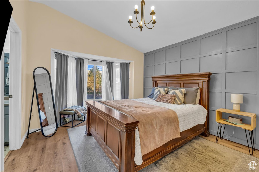 Bedroom with a chandelier, a decorative wall, light wood-type flooring, and lofted ceiling