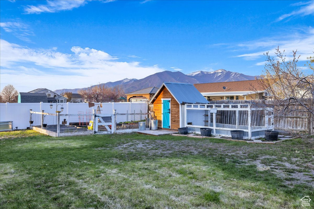 Back of house with a mountain view, a garden, a fenced backyard, and a lawn