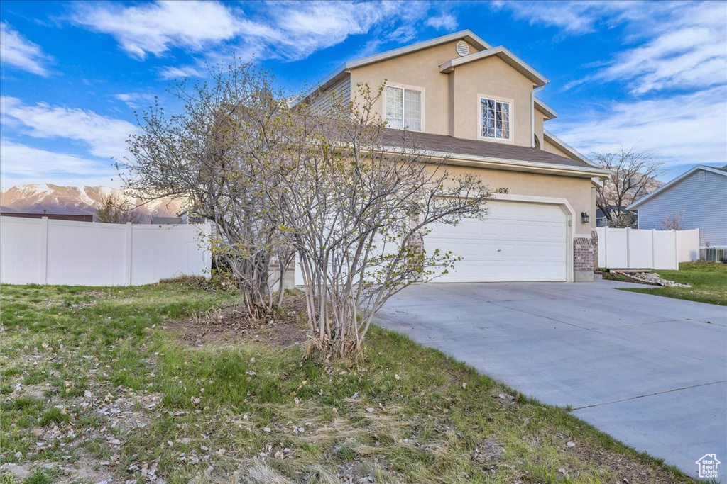 View of front facade with an attached garage, concrete driveway, stucco siding, and fence