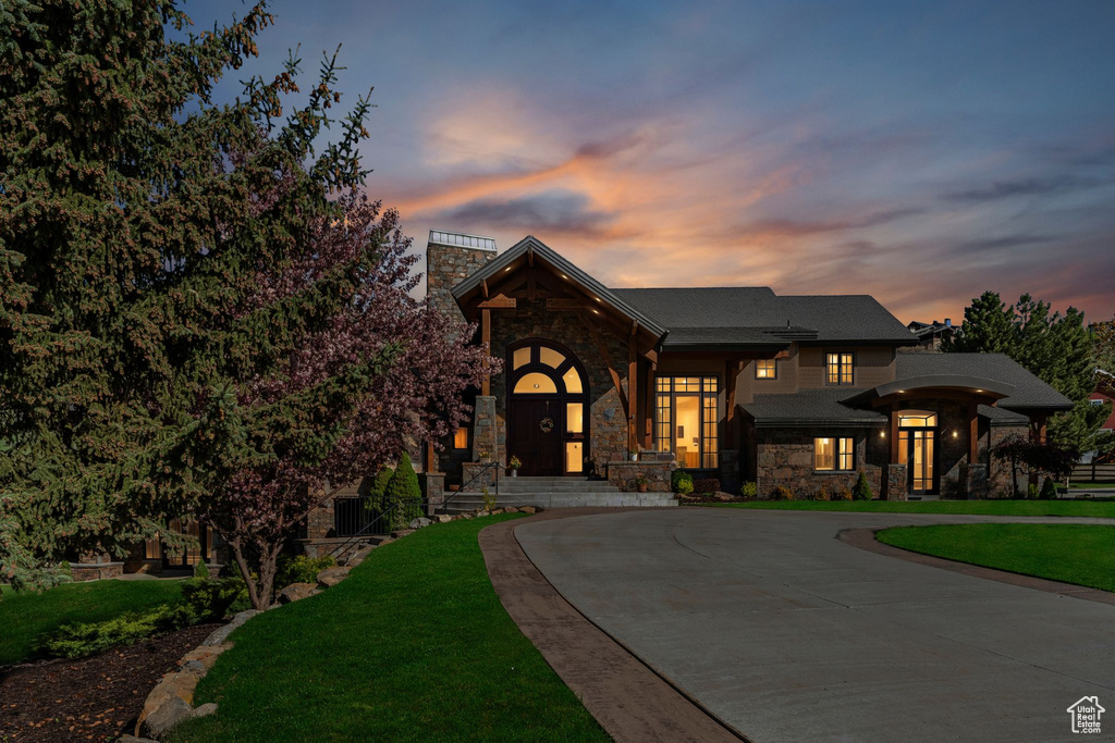 View of front facade with stone siding, curved driveway, a chimney, and a front yard