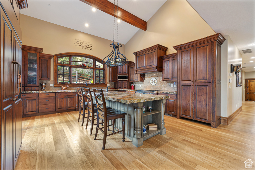 Kitchen with stainless steel microwave, light wood-style floors, tasteful backsplash, a center island with sink, and beam ceiling
