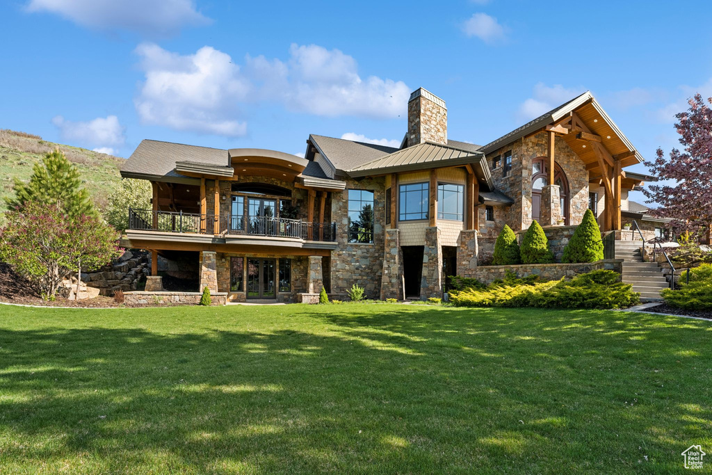 Back of house featuring stone siding, a balcony, a chimney, and a yard