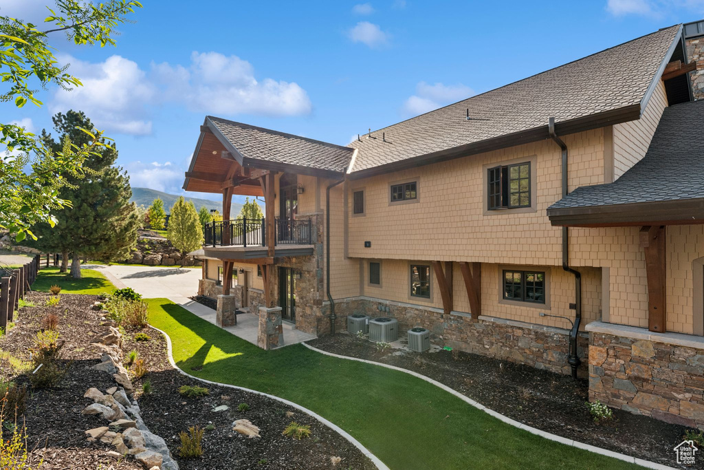 Back of property with a balcony, a patio, a yard, central AC unit, and roof with shingles