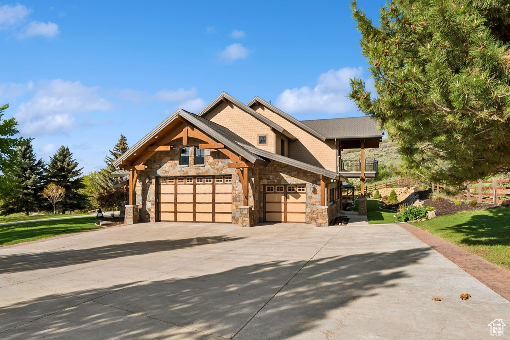 Craftsman-style home featuring stone siding, a balcony, concrete driveway, and a front lawn
