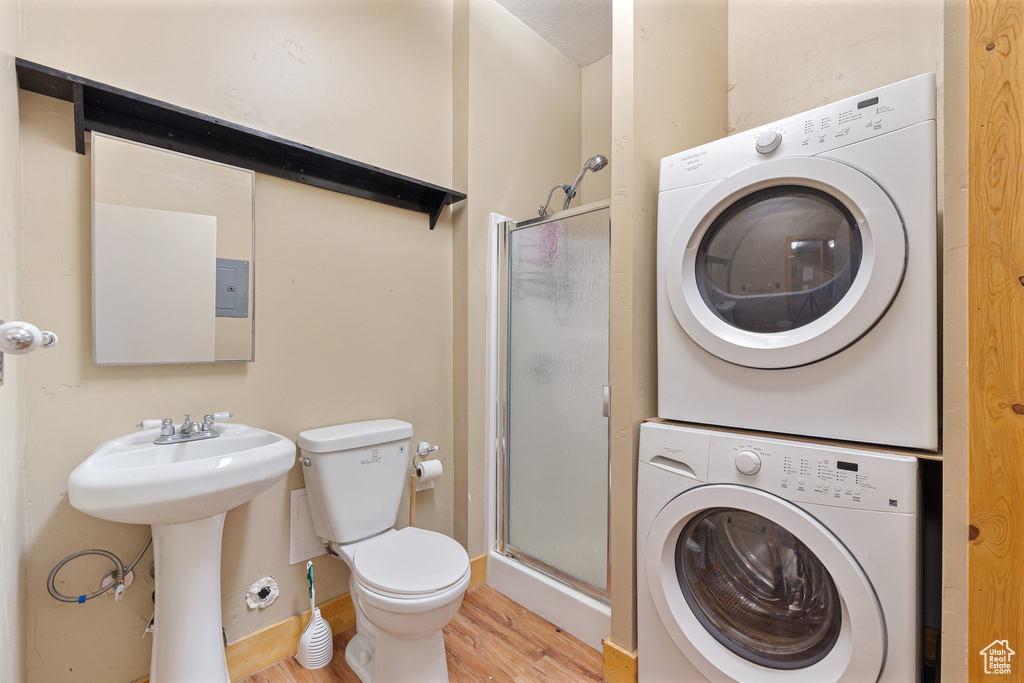 Bathroom featuring estacked washer and dryer, wood finished floors, a shower stall, and toilet