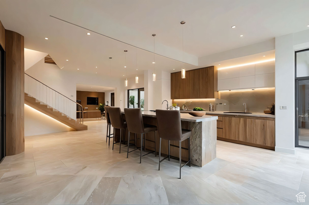 Kitchen with modern cabinets, light countertops, a large island with sink, open floor plan, and brown cabinetry