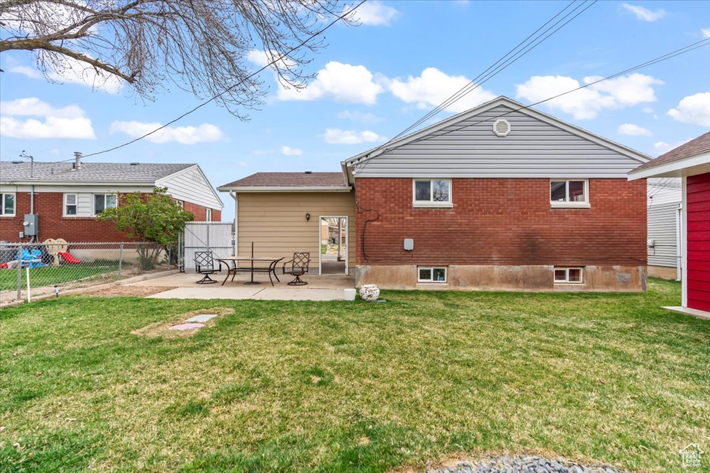Back of property featuring a patio area, brick siding, fence, and a lawn