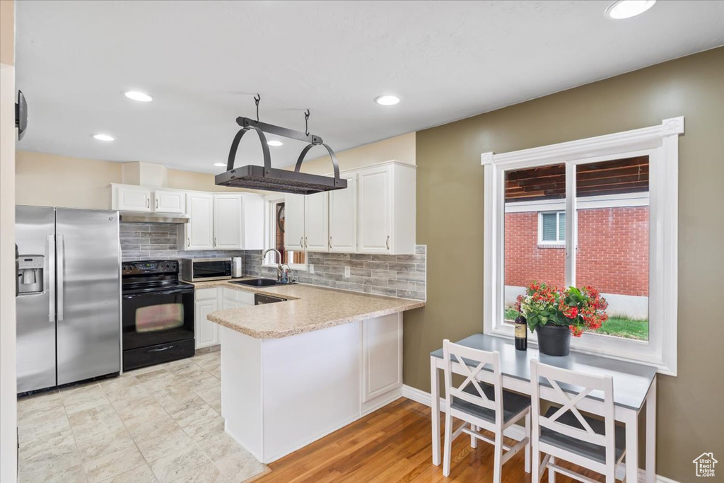 Kitchen with a peninsula, light countertops, white cabinetry, decorative backsplash, and appliances with stainless steel finishes