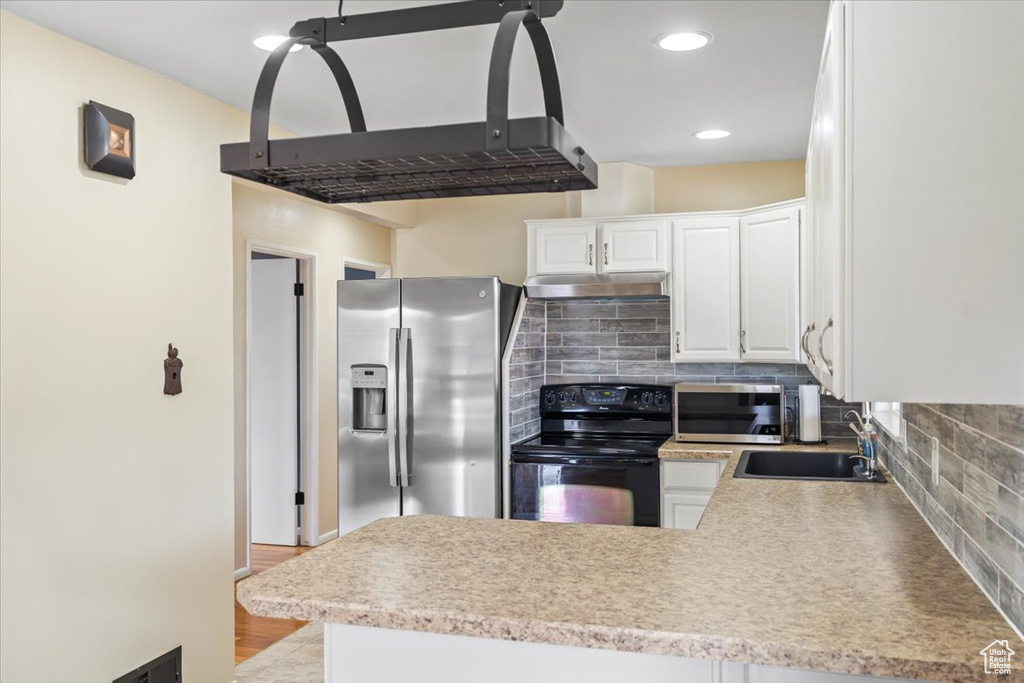 Kitchen featuring range hood, tasteful backsplash, a peninsula, appliances with stainless steel finishes, and a sink