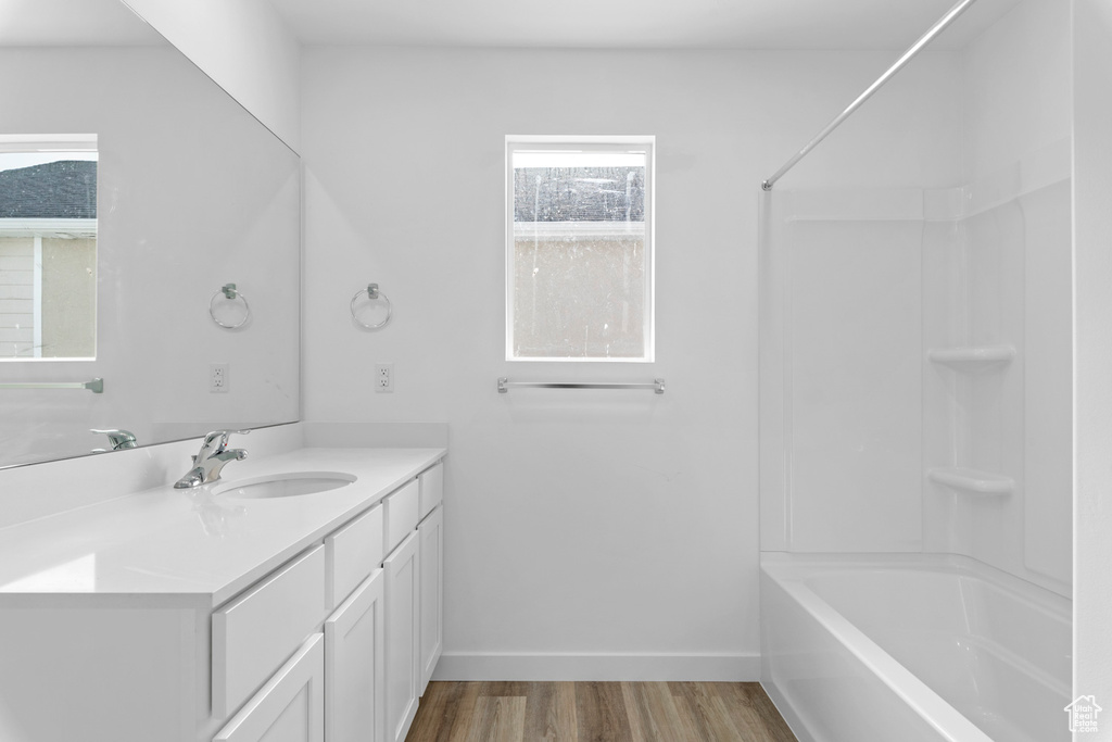 Bathroom with shower / tub combination, wood finished floors, vanity, and baseboards
