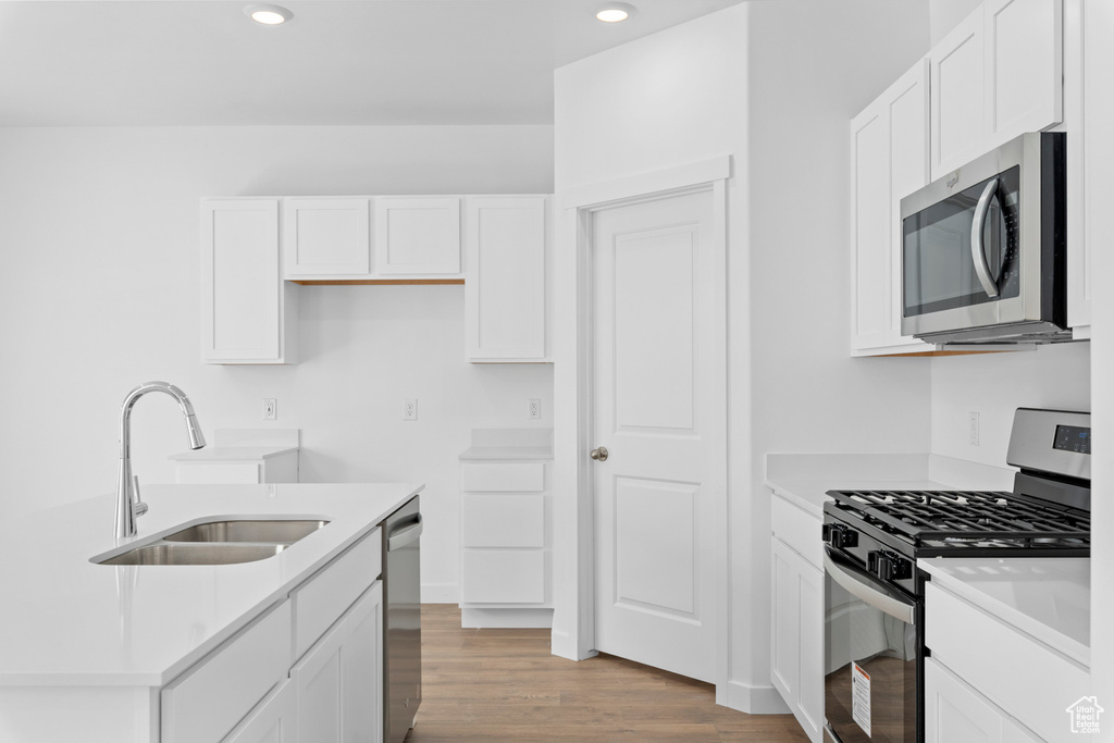 Kitchen featuring light wood-type flooring, appliances with stainless steel finishes, a sink, and white cabinetry