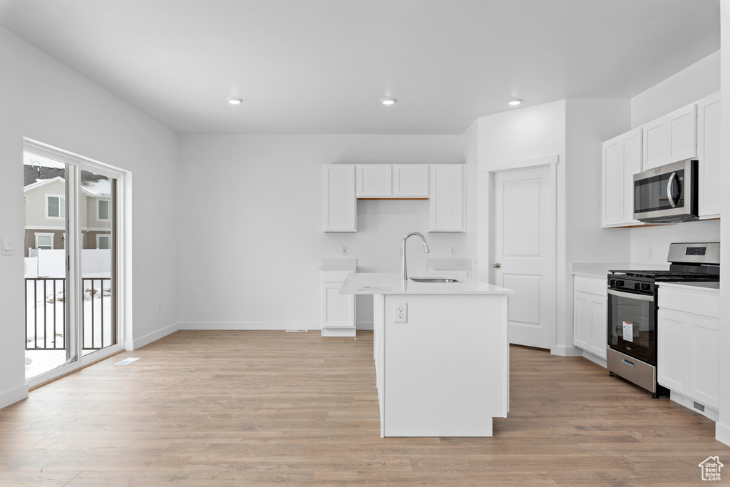 Kitchen featuring light wood-type flooring, appliances with stainless steel finishes, and an island with sink