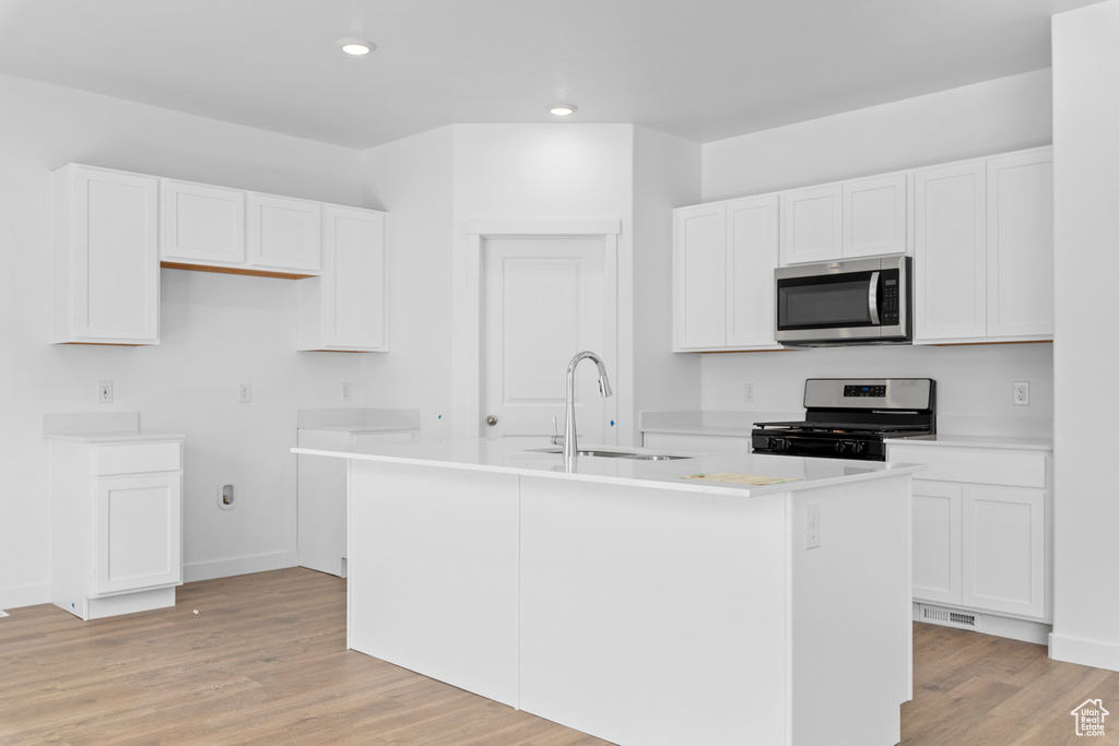 Kitchen with light wood-style flooring, white cabinetry, appliances with stainless steel finishes, a kitchen island with sink, and a sink