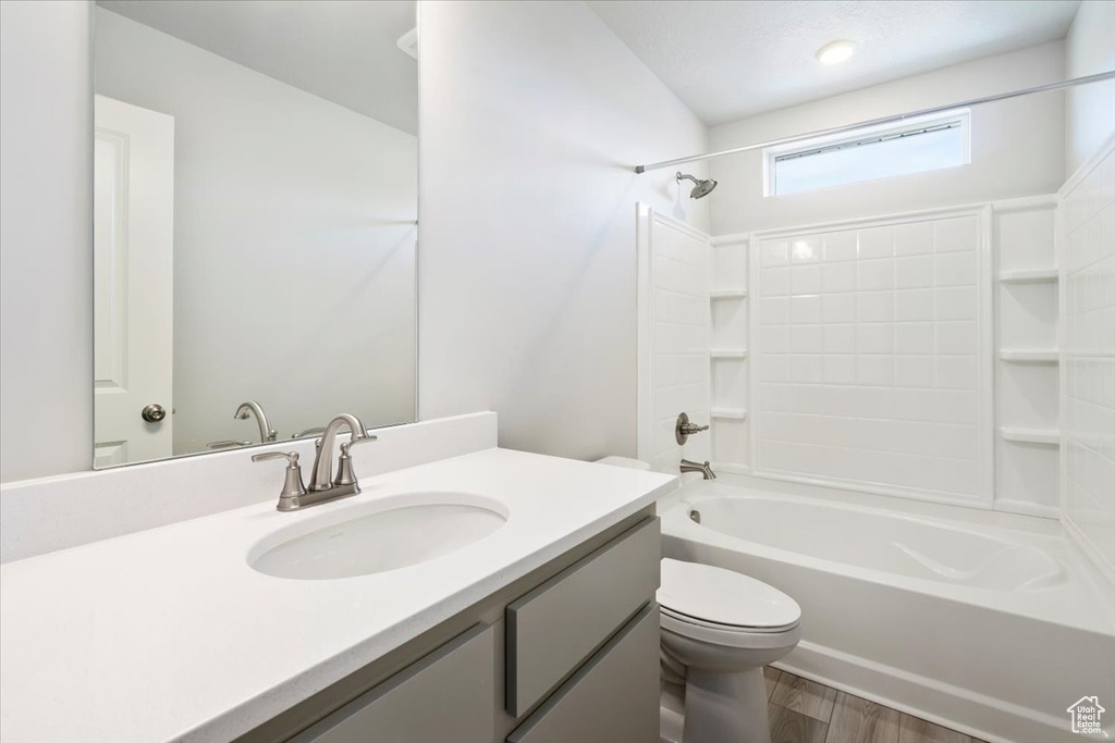 Bathroom with toilet, shower / bath combination, wood finished floors, and vanity