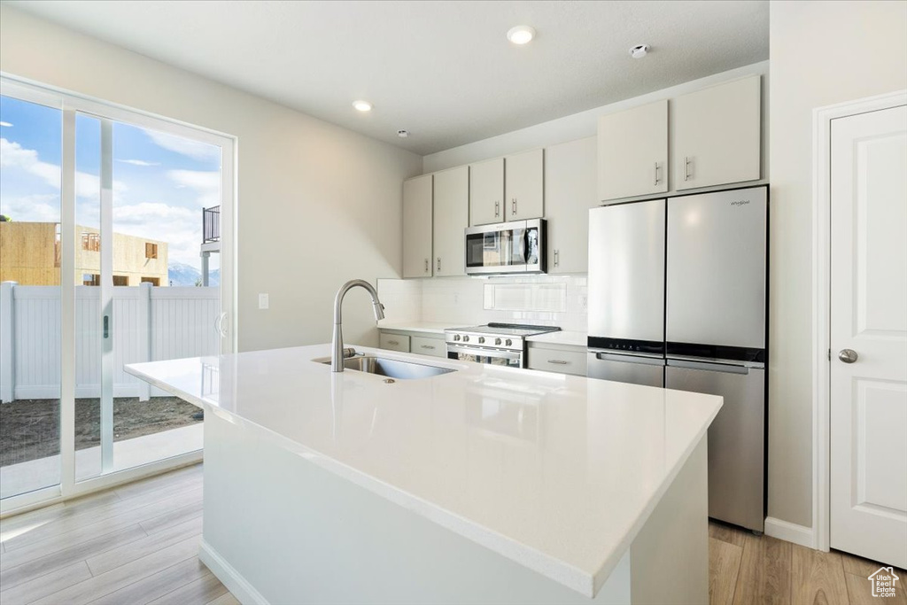 Kitchen with tasteful backsplash, light wood-type flooring, appliances with stainless steel finishes, a sink, and light countertops