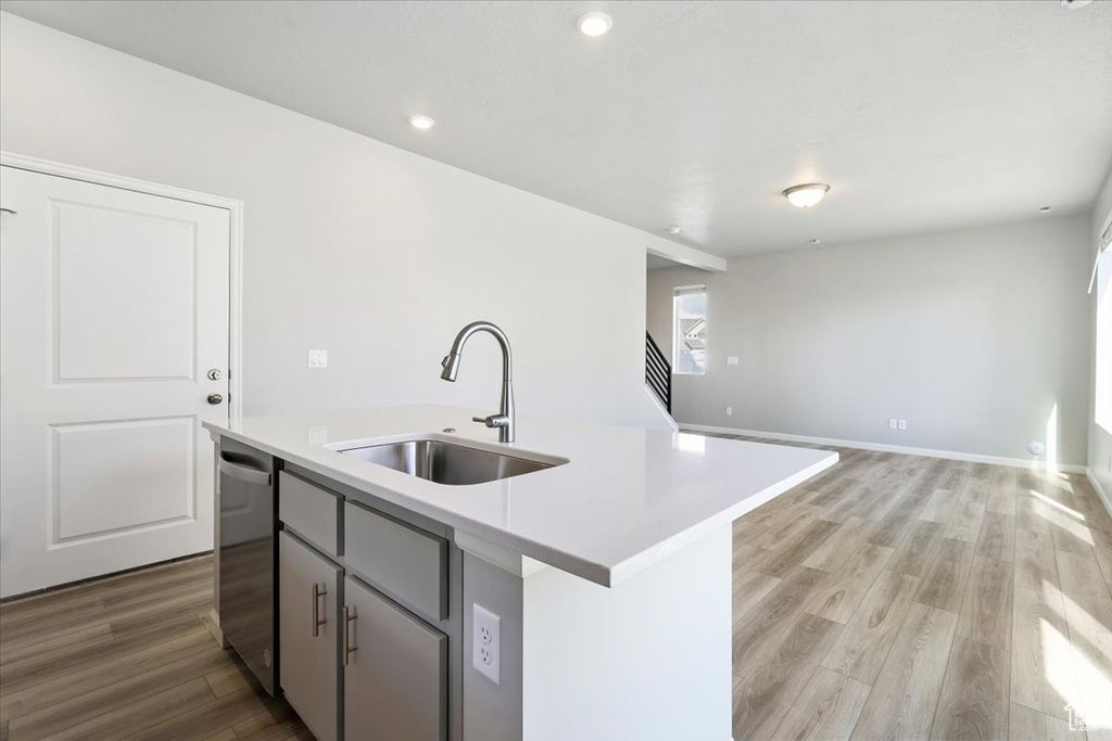 Kitchen featuring light countertops, a kitchen island with sink, light wood-style floors, stainless steel dishwasher, and a sink