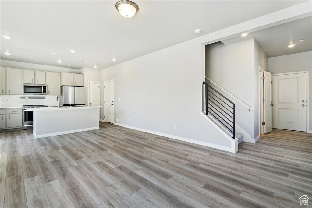 Unfurnished living room featuring recessed lighting, light wood-type flooring, stairway, and baseboards