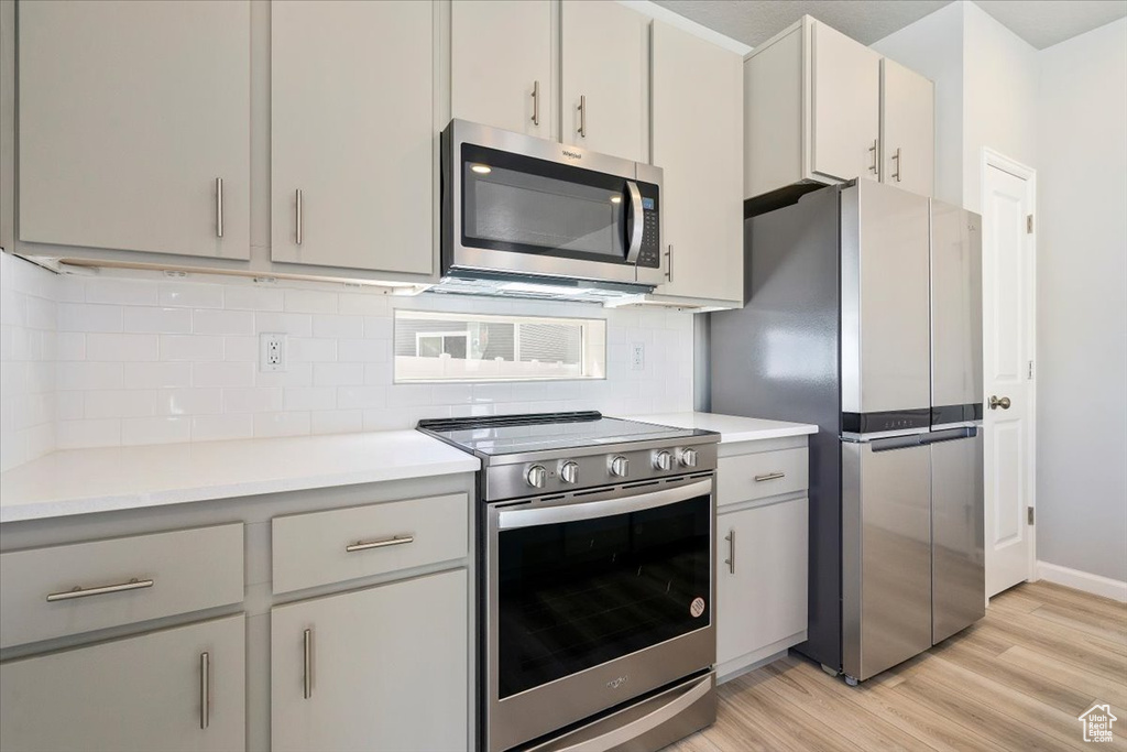 Kitchen with decorative backsplash, light wood-type flooring, light countertops, and appliances with stainless steel finishes