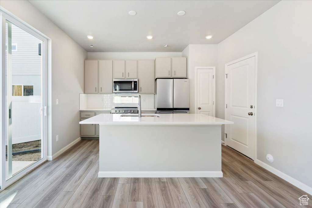 Kitchen featuring a kitchen island with sink, light countertops, a sink, stainless steel appliances, and light wood finished floors