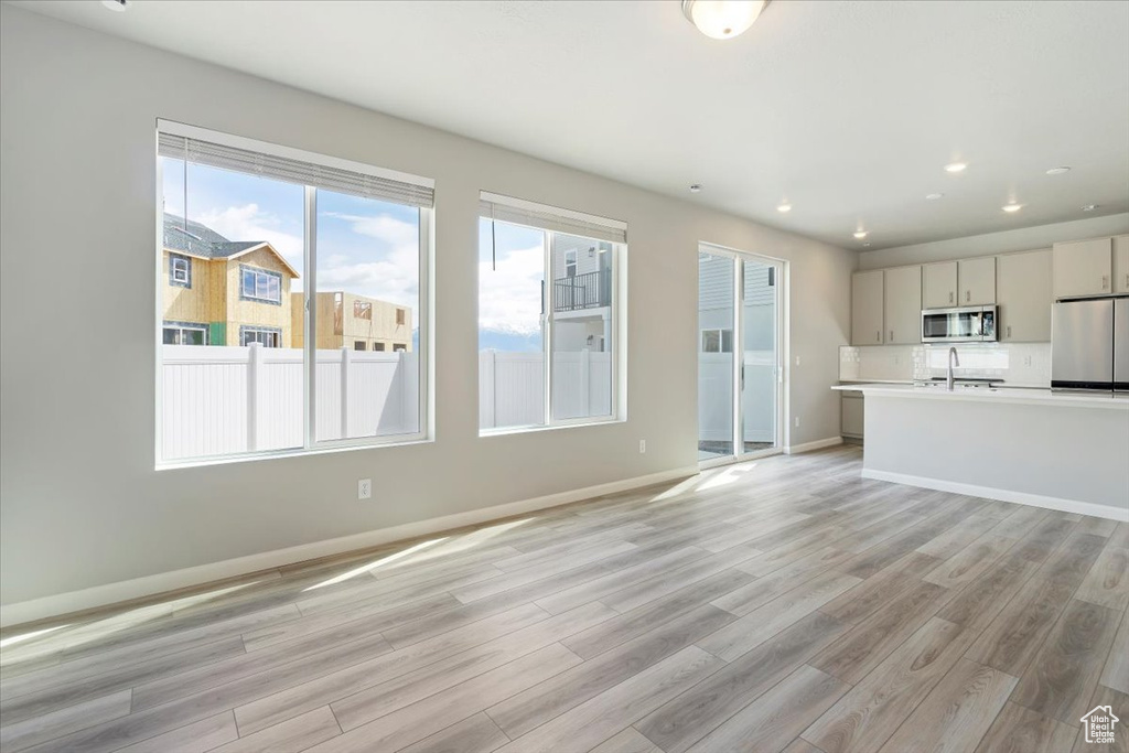 Unfurnished living room featuring a sink, baseboards, recessed lighting, and light wood-style floors
