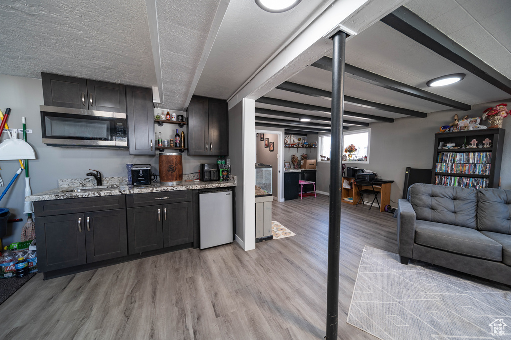 Bar with dishwashing machine, light wood-style flooring, indoor wet bar, stainless steel microwave, and a sink