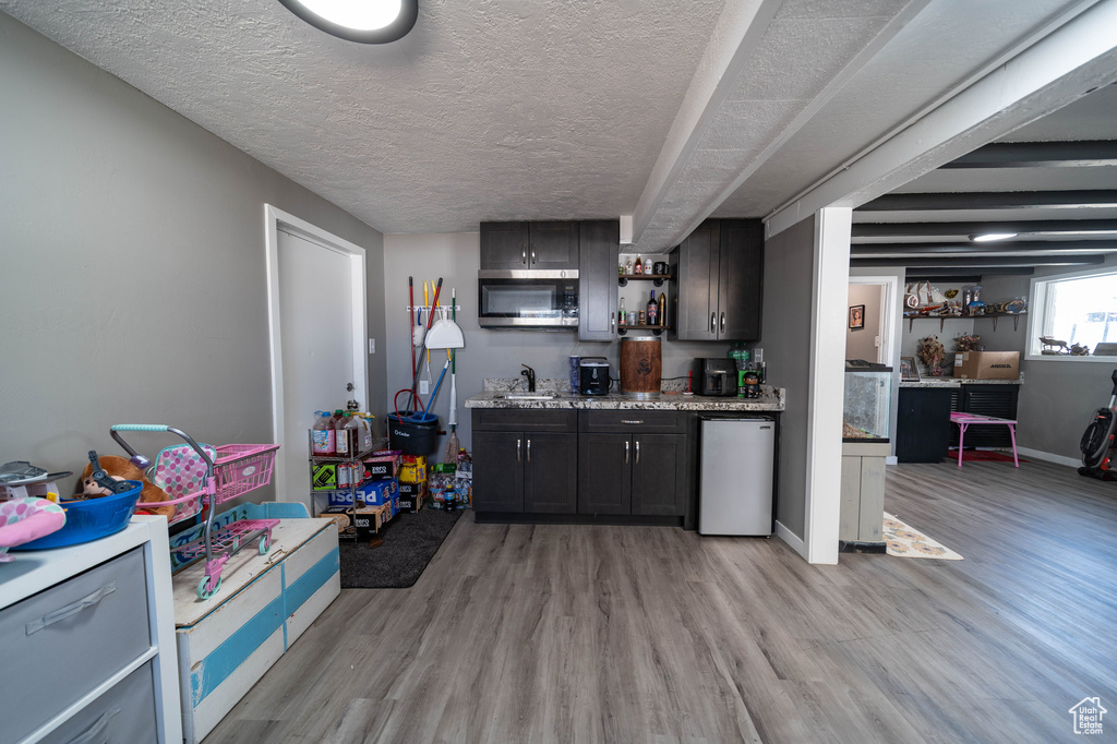 Bar with stainless steel microwave, refrigerator, wet bar, a textured ceiling, and light wood finished floors