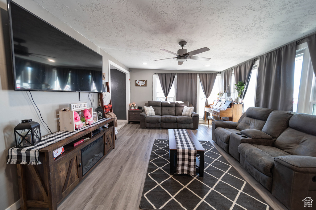 Living room with light wood-style flooring, a textured ceiling, ceiling fan, and baseboards