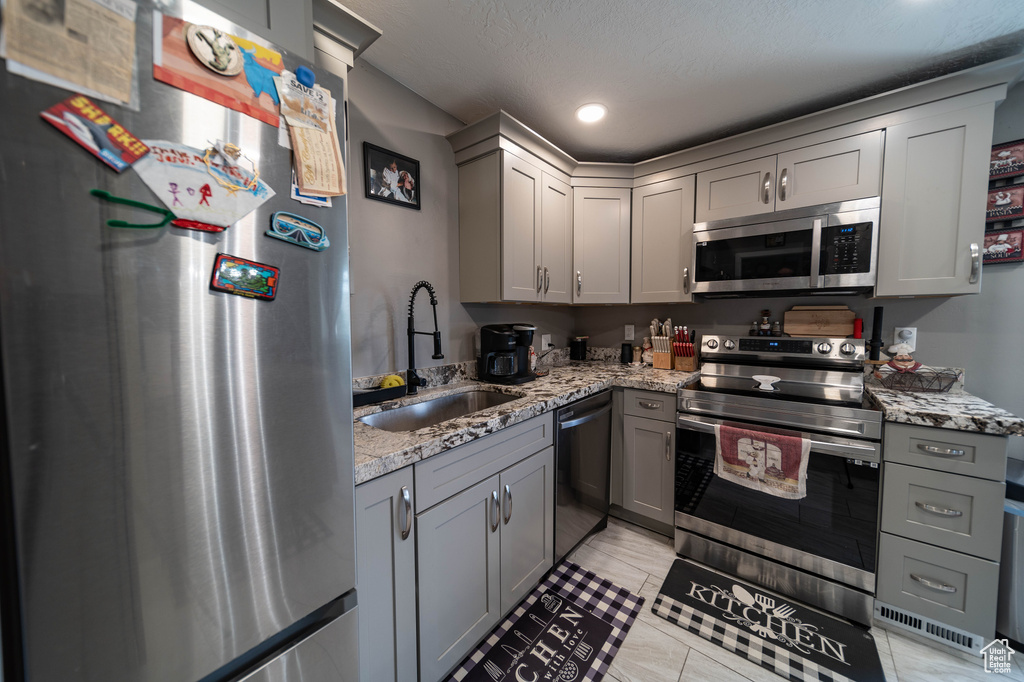 Kitchen featuring gray cabinets, appliances with stainless steel finishes, a sink, and light stone counters
