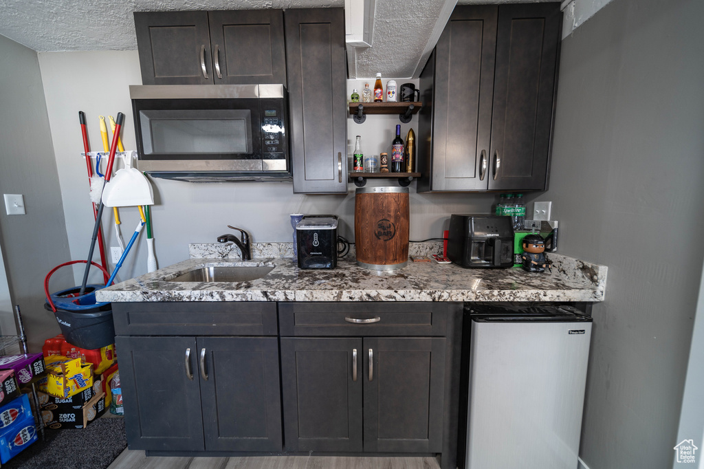 Kitchen featuring open shelves, a sink, a textured ceiling, stainless steel microwave, and refrigerator