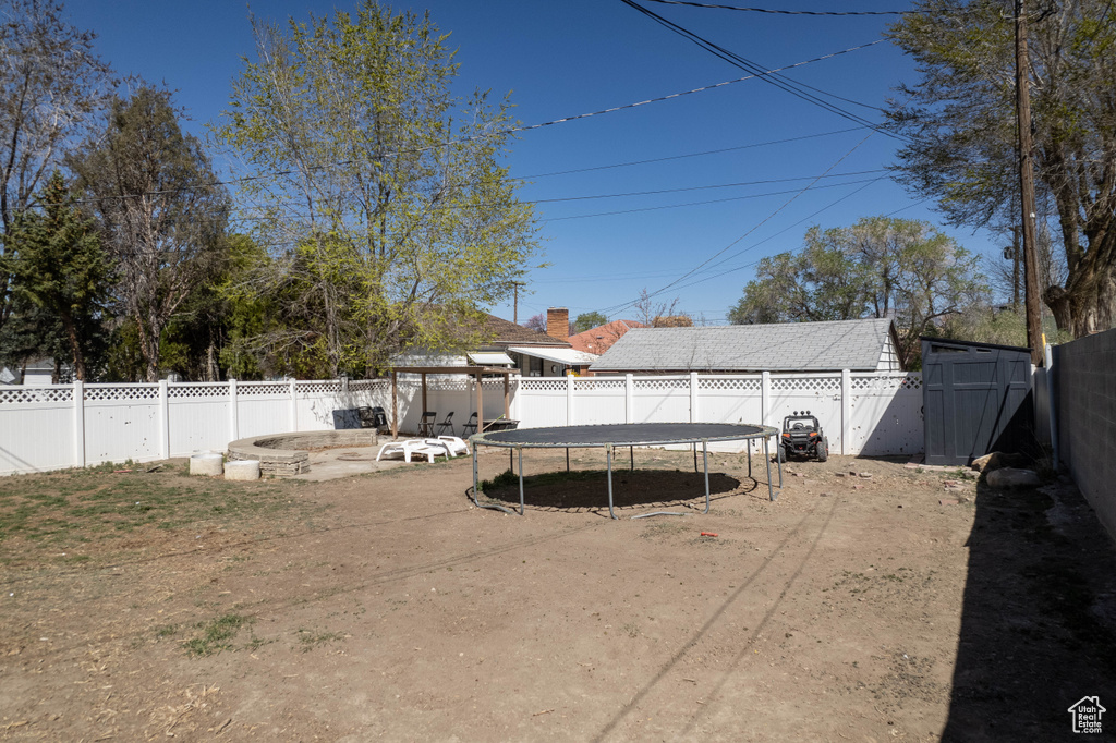 View of yard featuring a trampoline, a fenced backyard, an outbuilding, and a storage unit