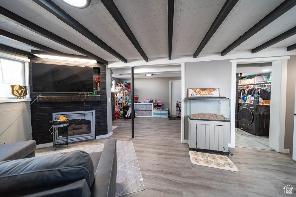 Living room featuring baseboards, beamed ceiling, wood finished floors, a large fireplace, and washing machine and clothes dryer
