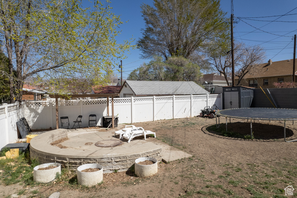 View of yard with a patio area, a trampoline, a fenced backyard, an outdoor structure, and a storage unit