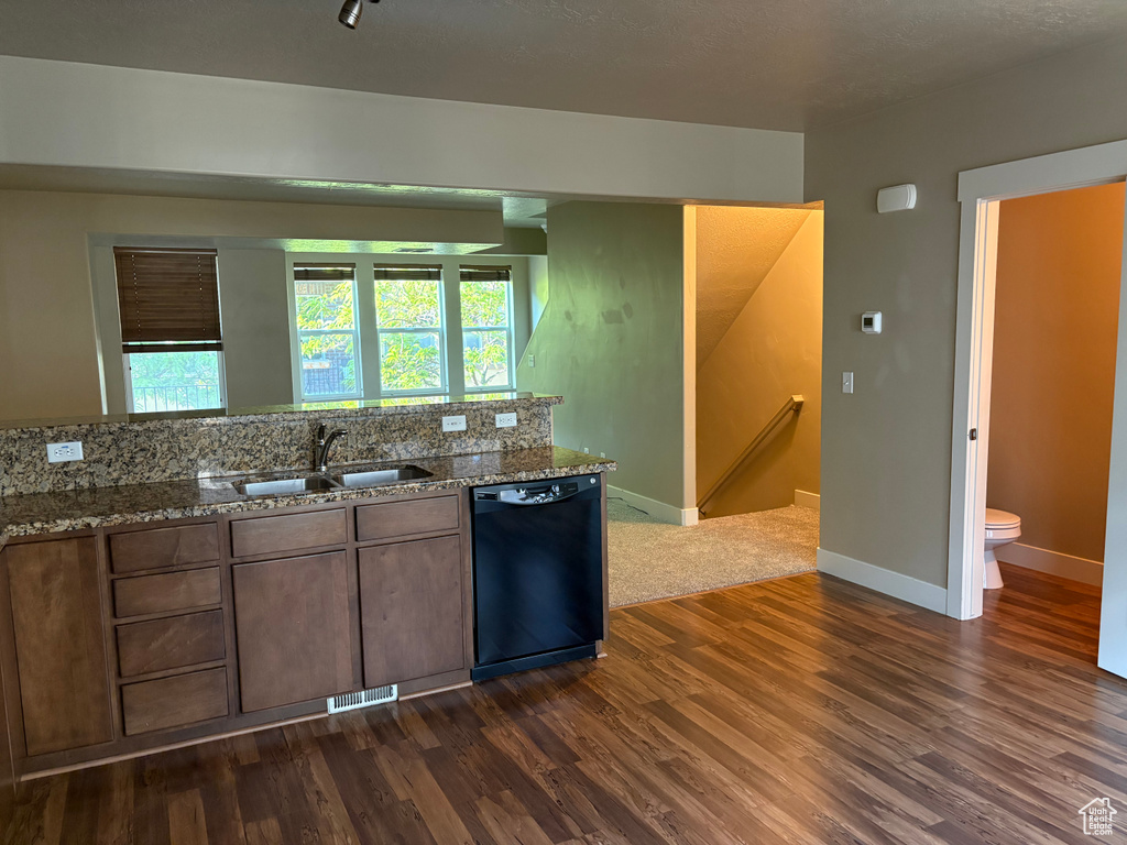 Kitchen featuring black dishwasher, a sink, dark wood-style flooring, stone counters, and baseboards