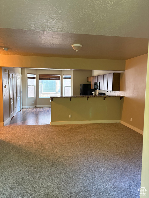 Unfurnished living room with carpet flooring, baseboards, and a textured ceiling