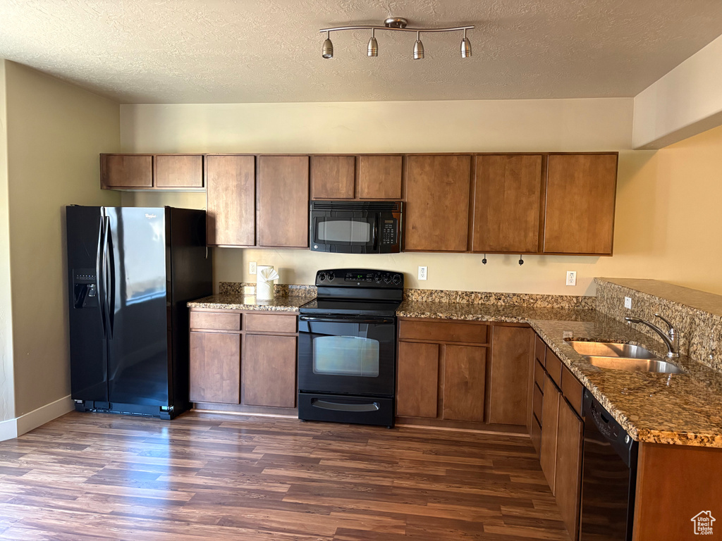 Kitchen featuring black appliances, dark wood-type flooring, a sink, brown cabinets, and dark stone countertops