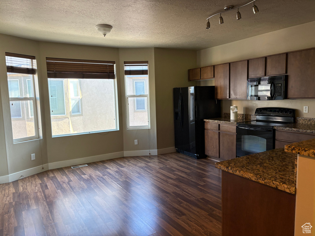 Kitchen featuring black appliances, dark countertops, dark wood-type flooring, baseboards, and a textured ceiling
