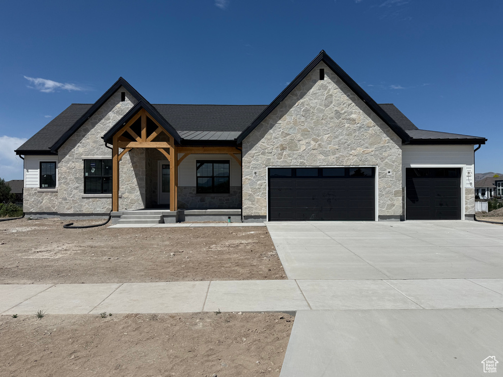View of front facade with stone siding, an attached garage, concrete driveway, and a porch