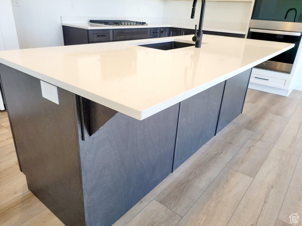 Kitchen featuring light countertops, a kitchen island with sink, gas stovetop, light wood finished floors, and a sink