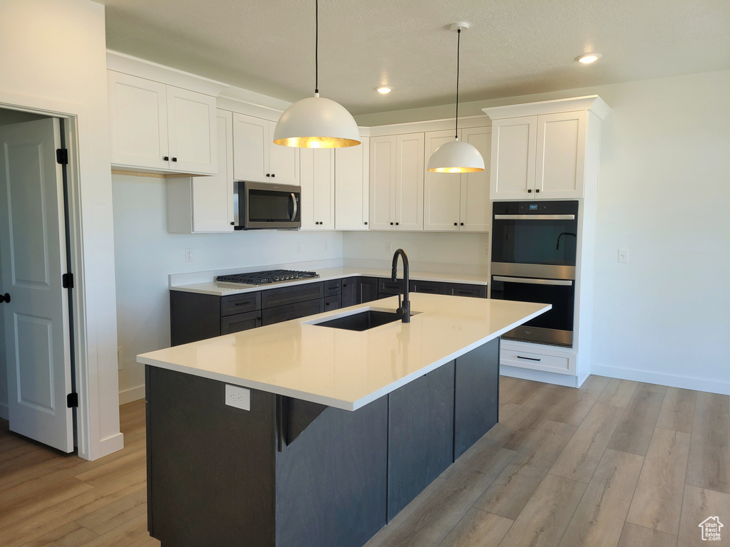 Kitchen featuring baseboards, decorative light fixtures, a sink, light wood-type flooring, and appliances with stainless steel finishes