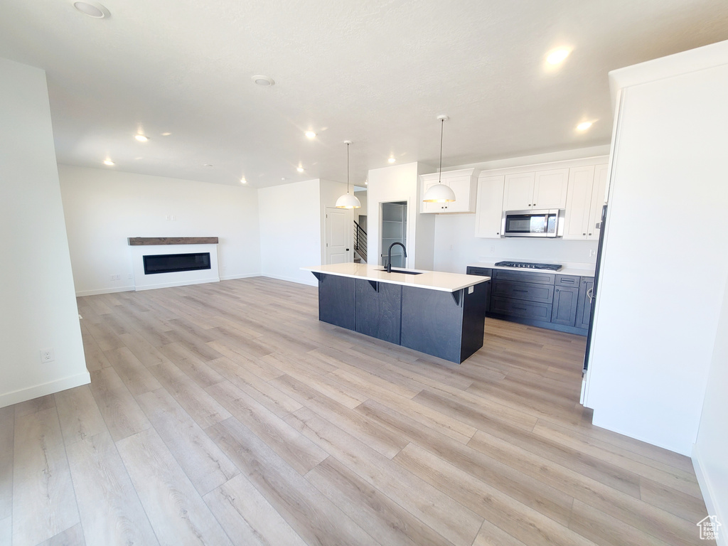Kitchen with open floor plan, light countertops, white cabinetry, light wood-style floors, and stainless steel appliances
