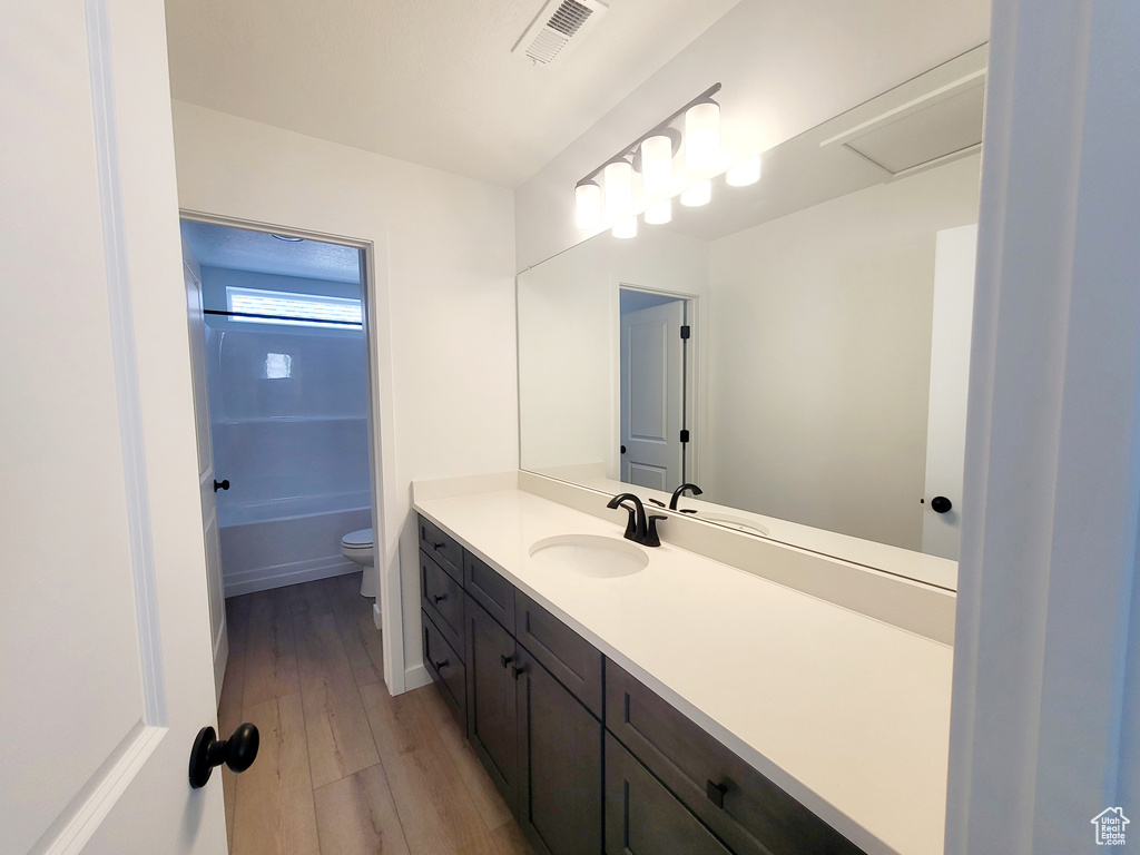 Full bathroom with visible vents, toilet, vanity, and wood finished floors