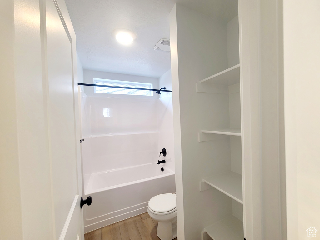 Bathroom with visible vents, washtub / shower combination, toilet, and wood finished floors
